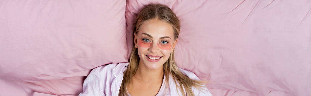 Widok z góry pozytywnej kobiety z przepaskami na oczy patrząc na kamerę na łóżku, baner  - Zdjęcie, obraz