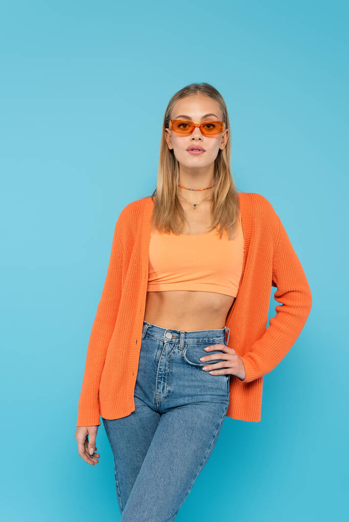 Blonde woman in sunglasses holding hand on hip isolated on blue  - Photo, Image