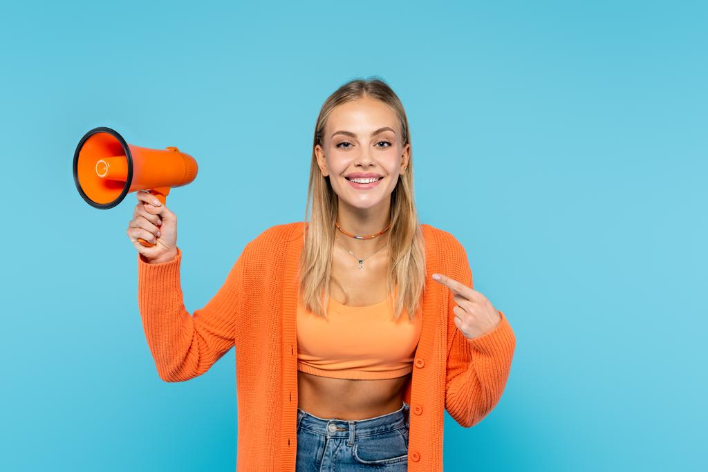 Lächelnde blonde Frau zeigt auf orangefarbenen Lautsprecher  - Foto, Bild