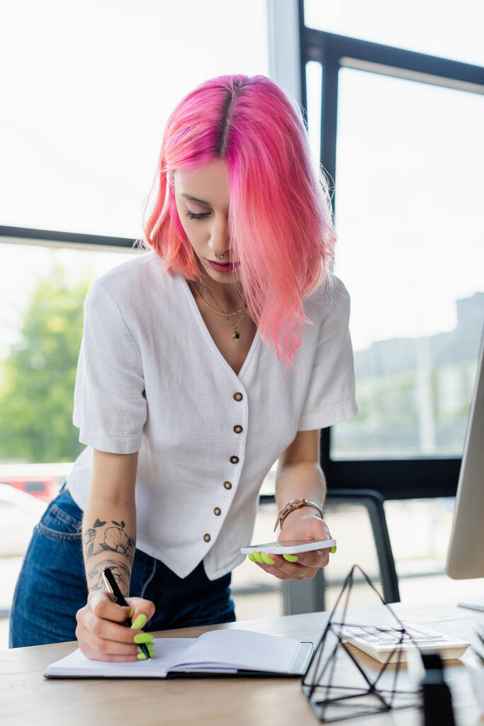 lävistetty nuori liikenainen vaaleanpunainen hiukset tilalla älypuhelin ja kirjallisesti muistikirja  - Valokuva, kuva