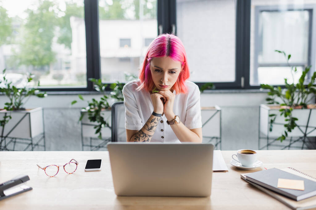 mujer de negocios enfocada con cabello rosa mirando a la computadora portátil en la oficina  - Foto, Imagen