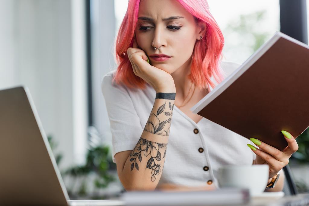 donna d'affari scontenta con cartella di tenuta dei capelli rosa e guardando il computer portatile - Foto, immagini