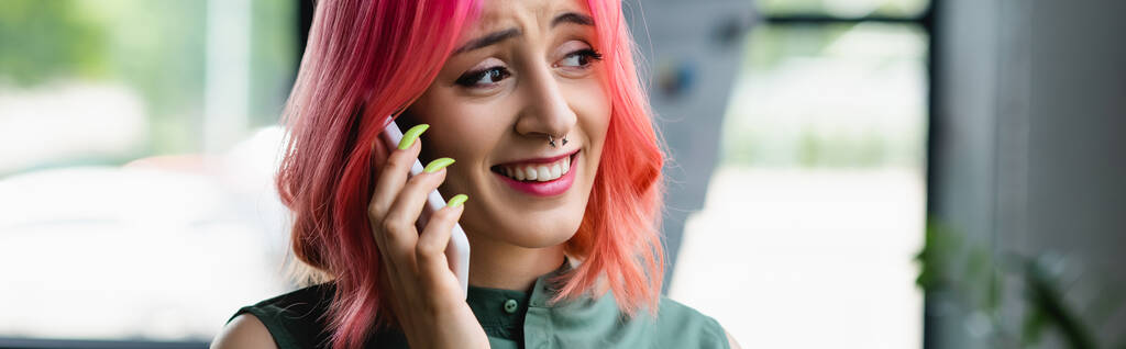 Positive Frau mit pinkfarbenen Haaren und piercenden Gesprächen auf Smartphone im Büro, Banner - Foto, Bild