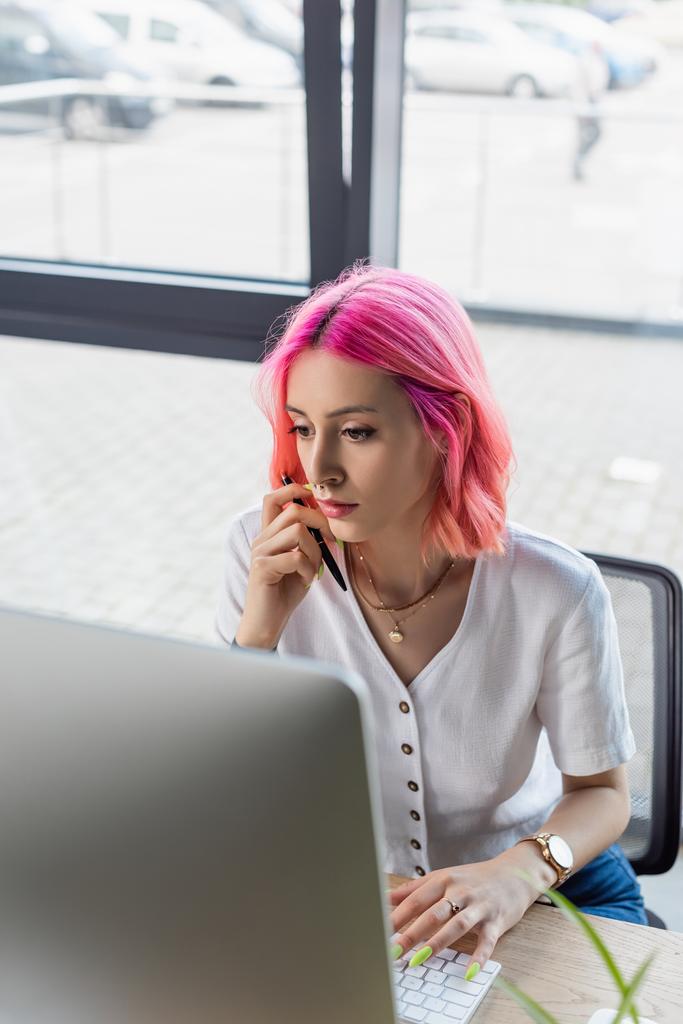 gerichte zakenvrouw met roze haar holding pen in de buurt van computer monitor  - Foto, afbeelding
