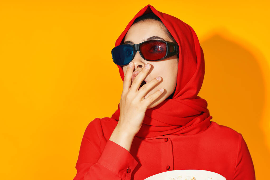 nő piros hidzsáb 3D szemüveg technológia néz film popcorn sárga háttér - Fotó, kép