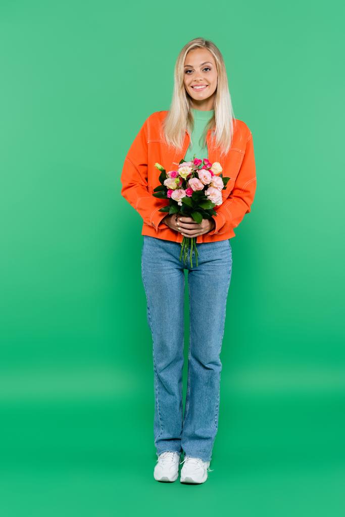 full length view of stylish blonde woman holding colorful bouquet on green - Photo, Image