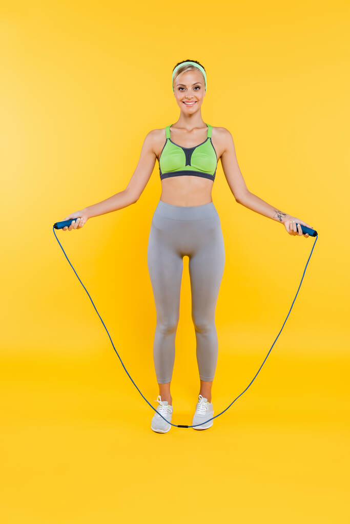 повний вигляд молодої жінки в спортивному одязі тренування зі стрибковою мотузкою на жовтому
 - Фото, зображення