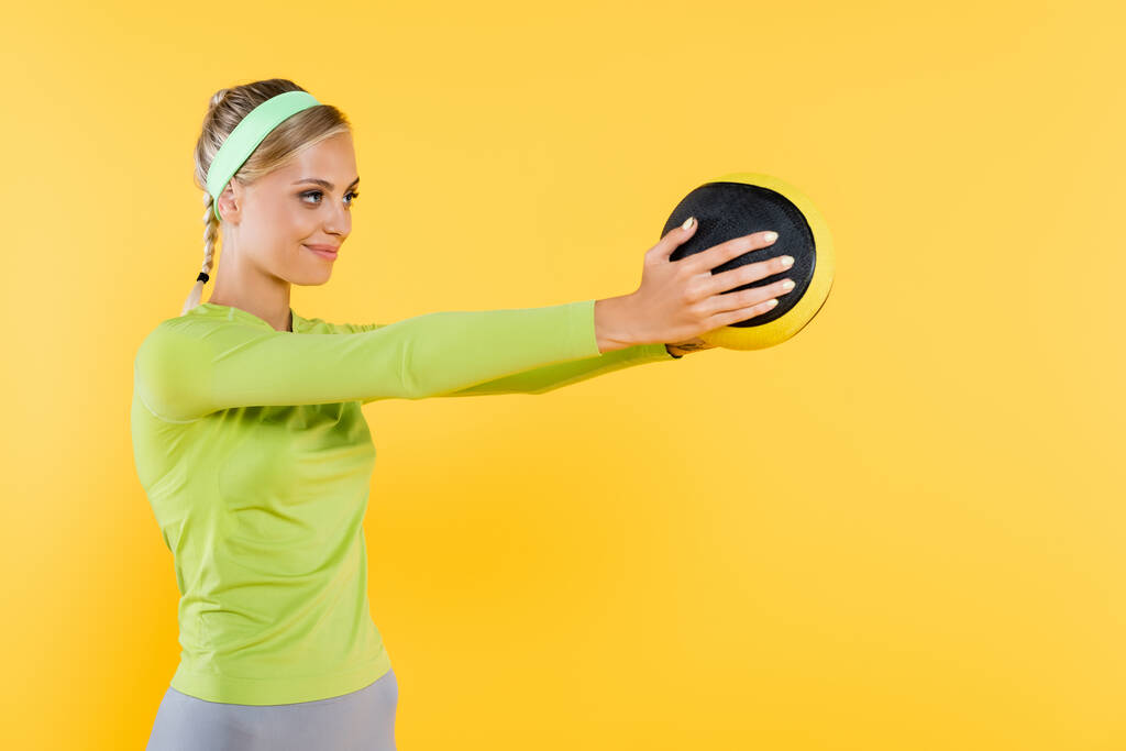 mujer feliz en verde camiseta de manga larga de entrenamiento con bola aislada en amarillo - Foto, imagen