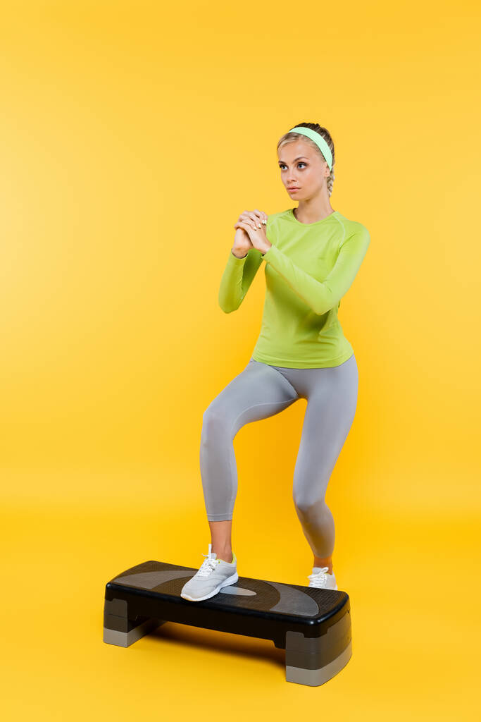 full length view of slim woman with clenched hands training on step board on yellow - Photo, Image