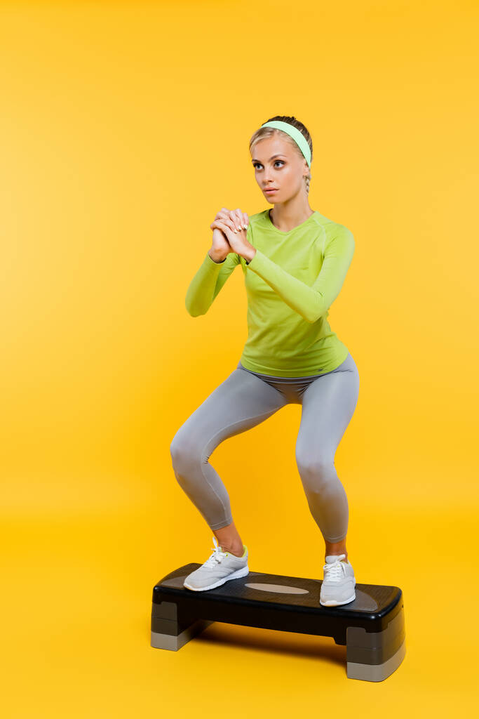 Αθλητική γυναίκα με σφιγμένα χέρια κάνει sit ups στον πίνακα βήμα σε κίτρινο - Φωτογραφία, εικόνα
