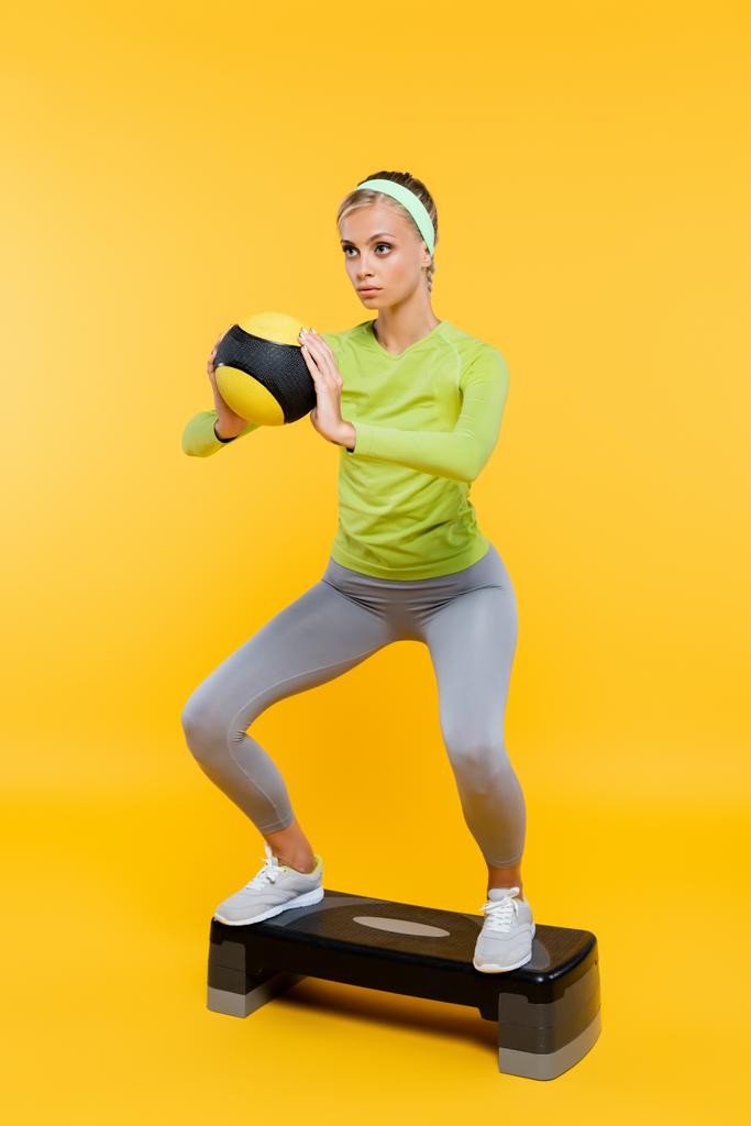 mulher em sportswear segurando bola ao fazer sit ups no trampolim em amarelo - Foto, Imagem