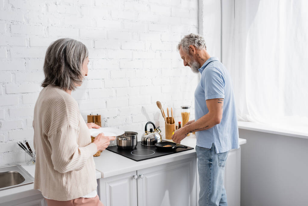 Homme mûr cuisine crêpe près de femme avec assiette dans la cuisine  - Photo, image