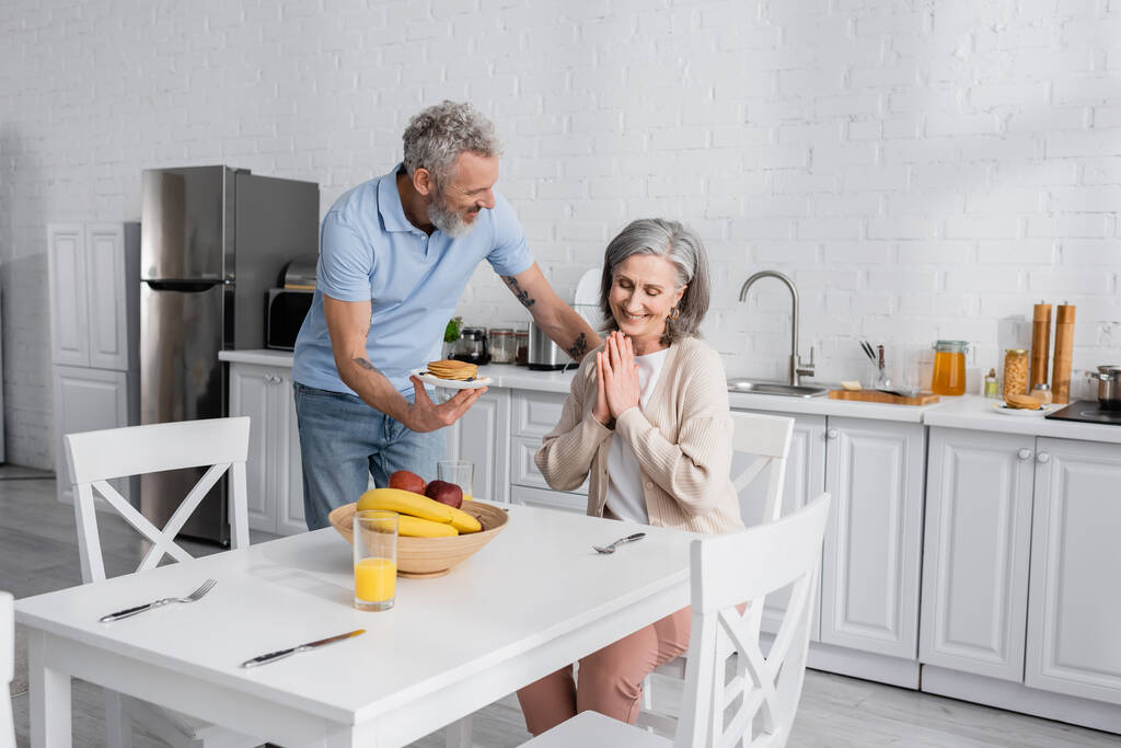 Fröhlich ein Pfannkuchen halten neben Frau und Obst in der Küche  - Foto, Bild