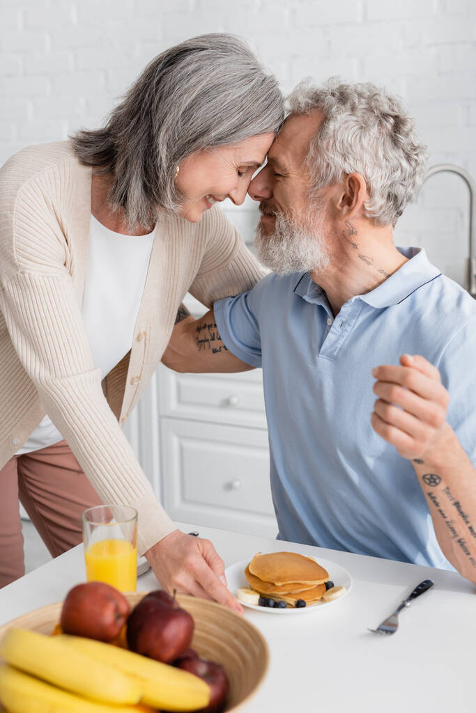 Seitenansicht eines lächelnden Paares beim Frühstück in der Küche. Übersetzung: "Man muss tiefe Brunnen graben, wenn man klares Wasser will." - Foto, Bild