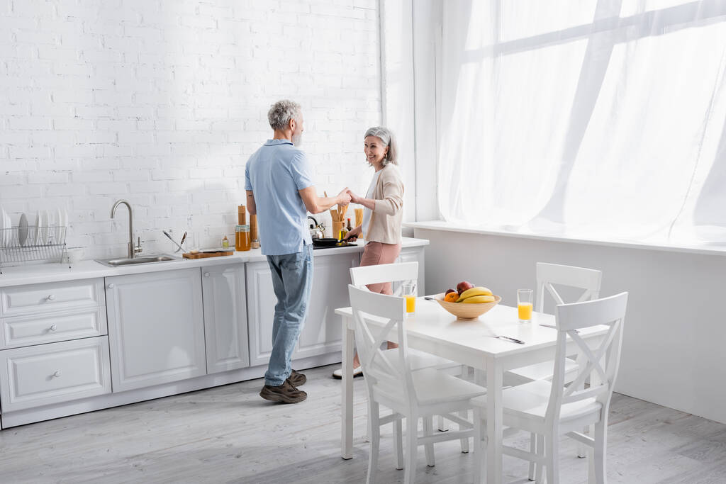 Sourire couple d'âge mûr tenant la main tout en cuisinant dans la cuisine - Photo, image