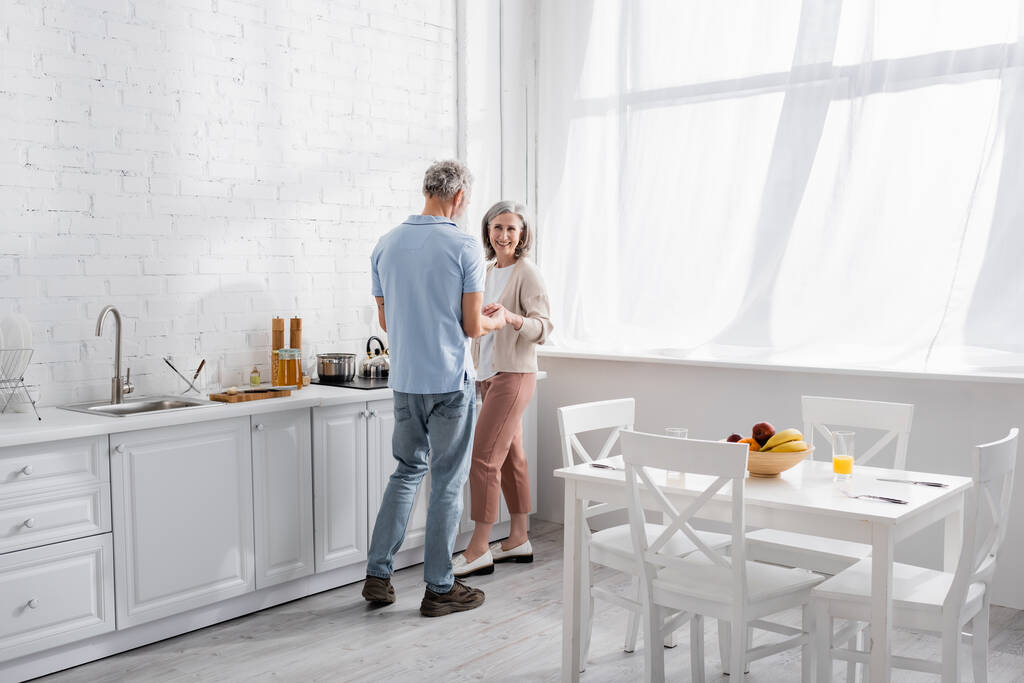 Reifer Mann hält Hand lächelnder Frau in der Nähe von Arbeitsplatte in Küche  - Foto, Bild