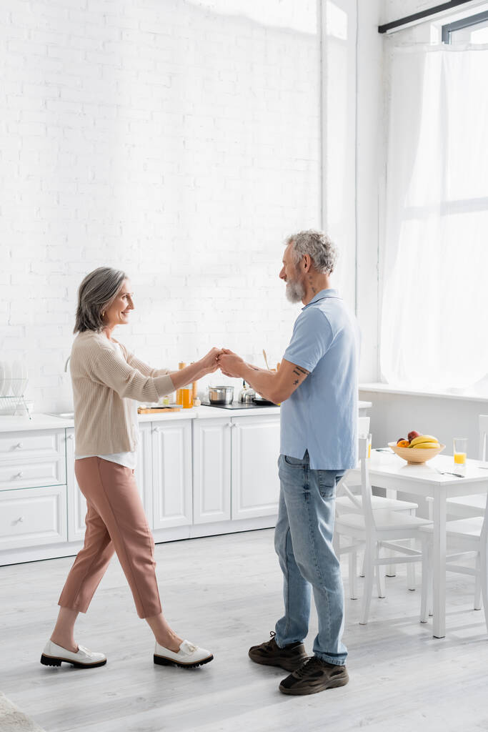 Vue latérale du couple d'âge moyen dansant près des fruits et du jus d'orange sur la table  - Photo, image
