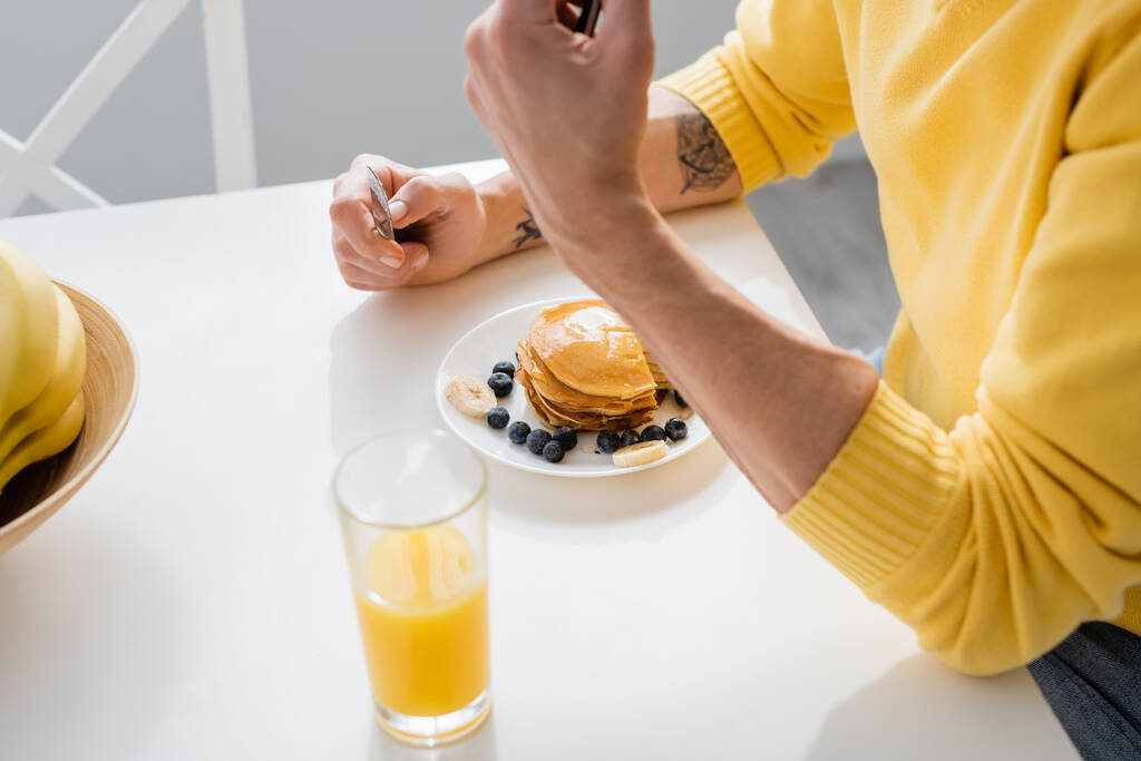 Widok dojrzałego mężczyzny trzymającego nóż w pobliżu naleśników i soku pomarańczowego w kuchni  - Zdjęcie, obraz