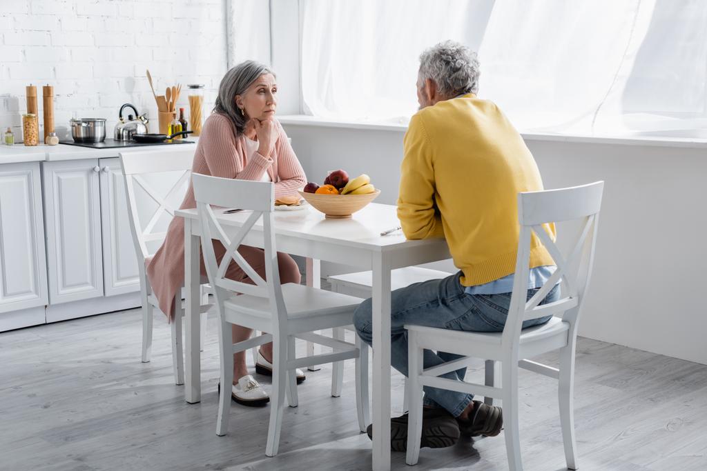 Mature woman looking at husband near breakfast in kitchen  - Photo, Image
