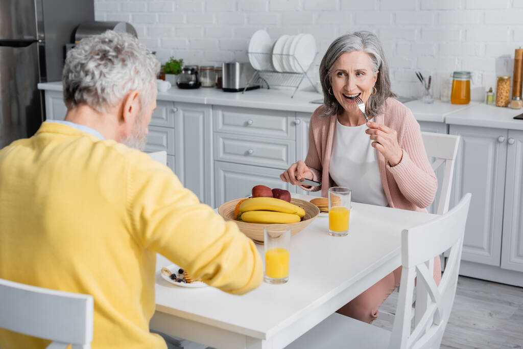 Kocasıyla mutfakta kahvaltı ederken krep yiyen olgun bir kadın.  - Fotoğraf, Görsel