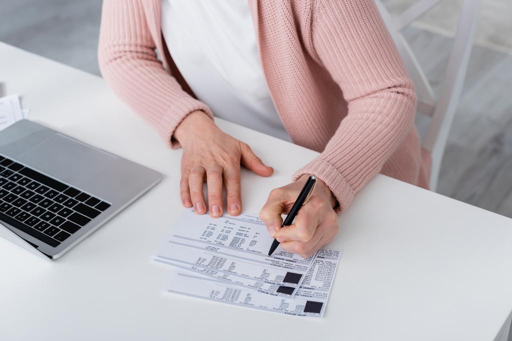 Обрезанный вид женщины, пишущей на счет возле ноутбука дома  - Фото, изображение
