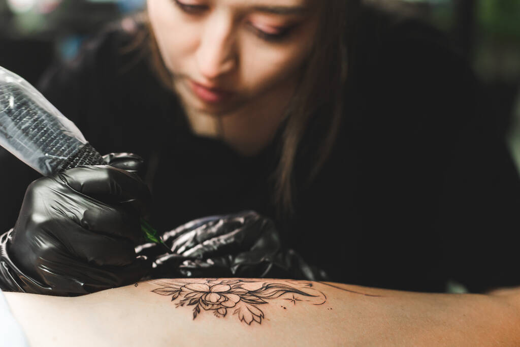 Kadın dövme sanatçısı stüdyoda dövme yapıyor, vücudunda dövme yapıyor. Yakın çekim - Fotoğraf, Görsel