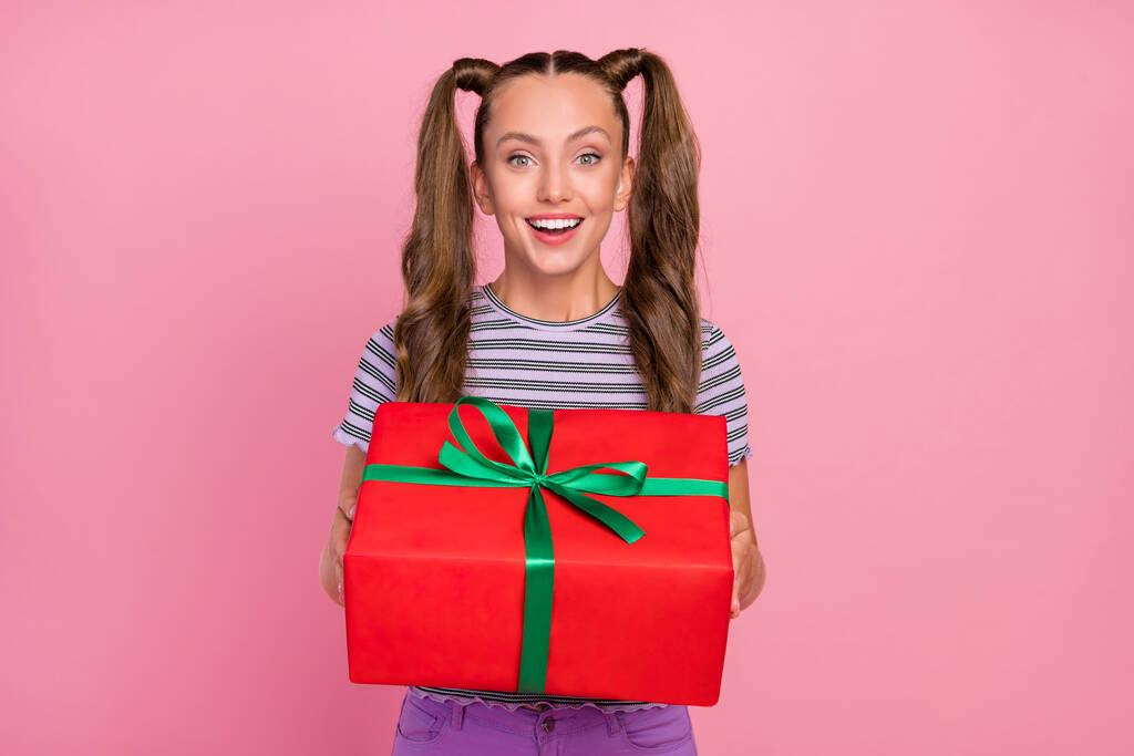 Портрет привлекательной веселой длинноволосой девушки, держащей в руках праздничный большой ящик, изолированный на розовом фоне - Фото, изображение