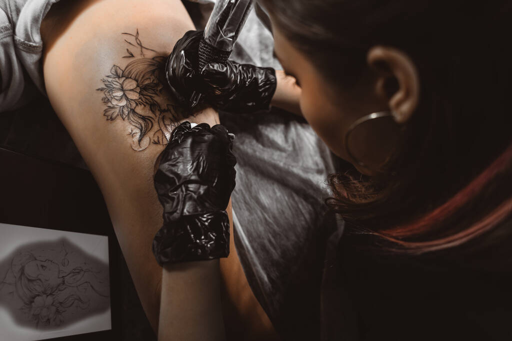 tekening van een tatoeage op het been van dichtbij. Vrouw tatoeage kunstenaar maakt een tekening met een speciale machine in een kunststudio - Foto, afbeelding