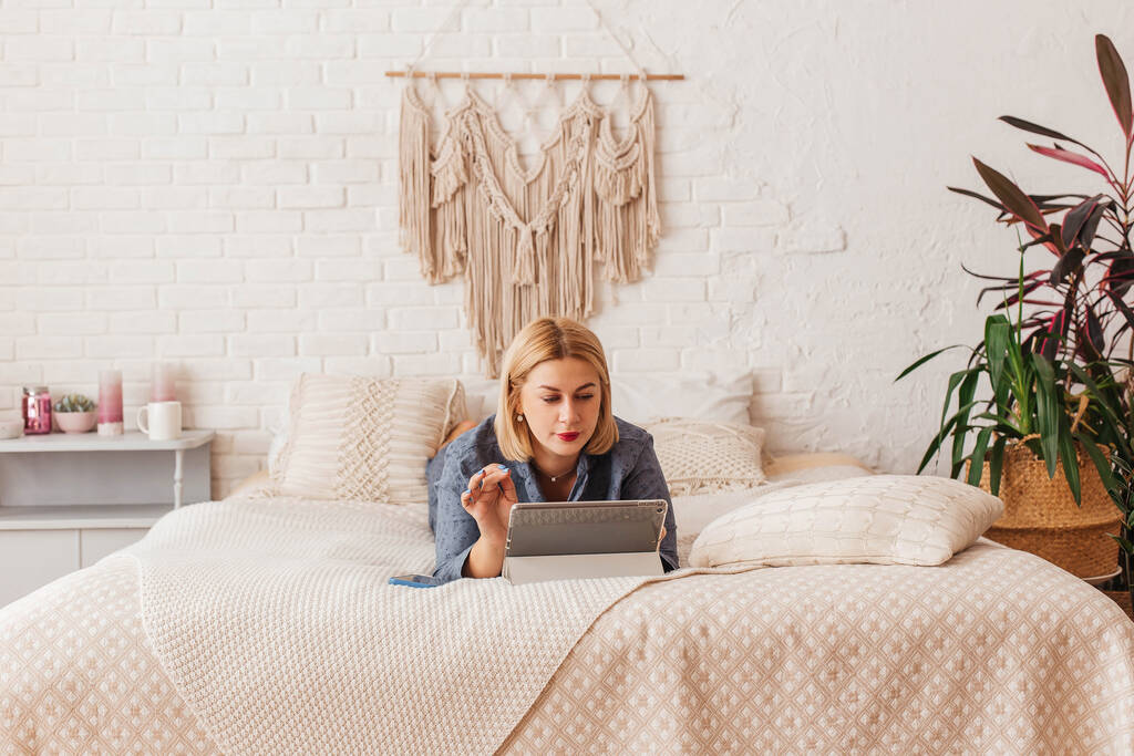 Beautiful young woman in pajamas, working on a laptop in bed, talking on the phone. Online shopping - Photo, Image
