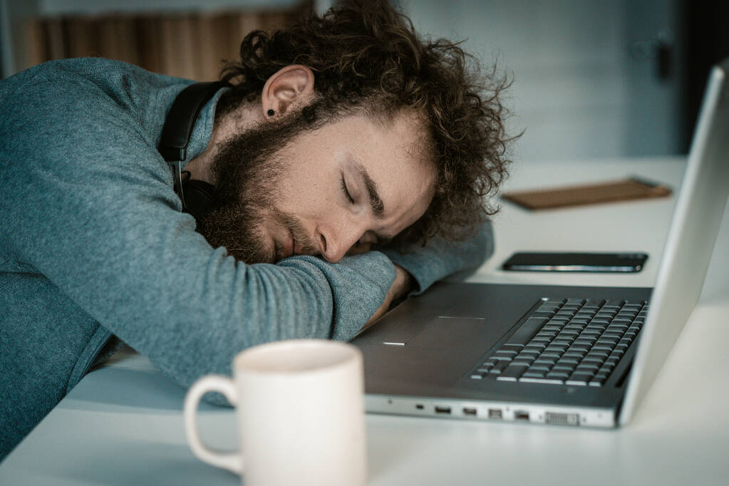 Homem com as mãos dobradas dorme na mesa com laptop. Dormir sentado, Freelance à noite, caneca de café na mesa. Close-up - Foto, Imagem