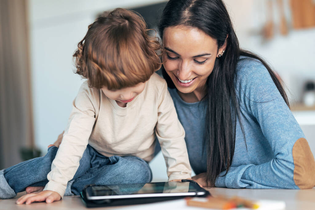 Laukaus nuori hymyilevä äiti ja hänen söpö poikansa katsomassa sarjakuvia digitaalinen tabletti keittiössä kotona. - Valokuva, kuva