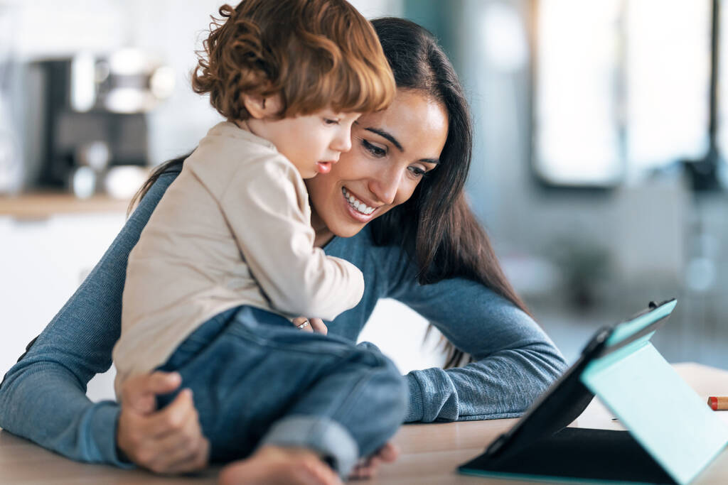 Съемка молодой улыбающейся матери и ее милый сын смотреть мультфильмы на цифровой планшет на кухне дома. - Фото, изображение