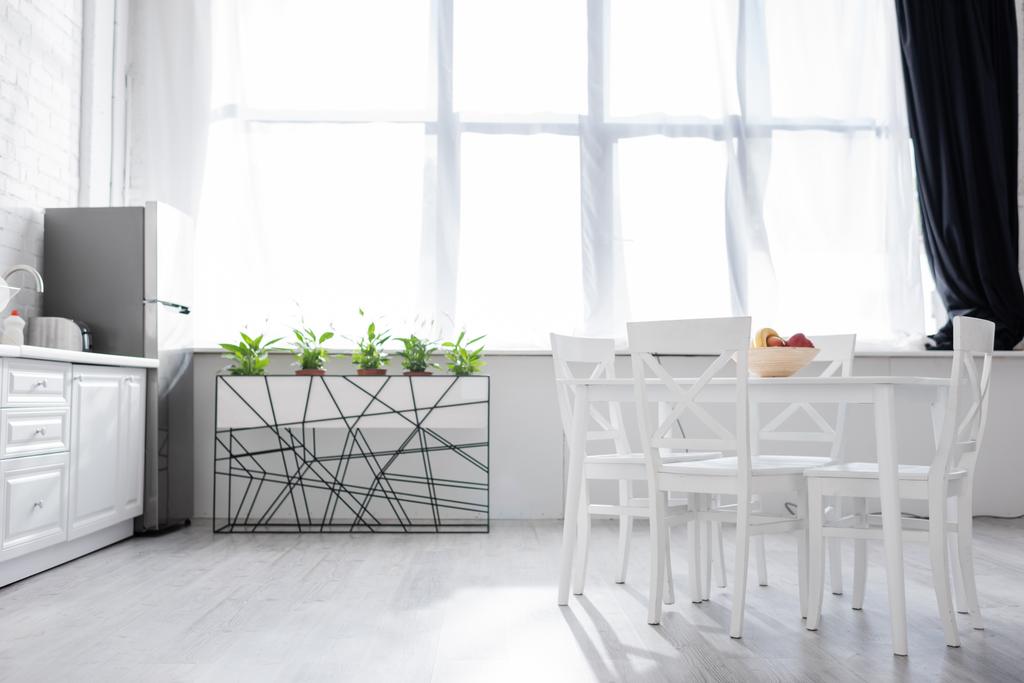 τραπέζι με φρούτα κοντά σε λευκές καρέκλες στη σύγχρονη κουζίνα  - Φωτογραφία, εικόνα