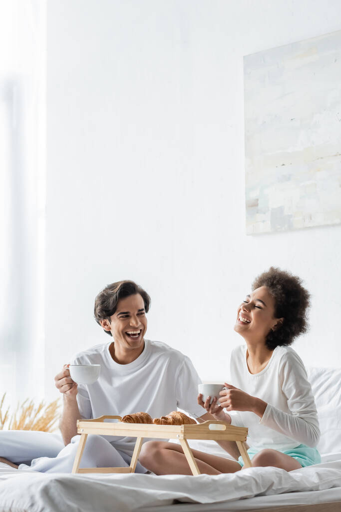 alegre interracial pareja teniendo desayuno en cama  - Foto, Imagen
