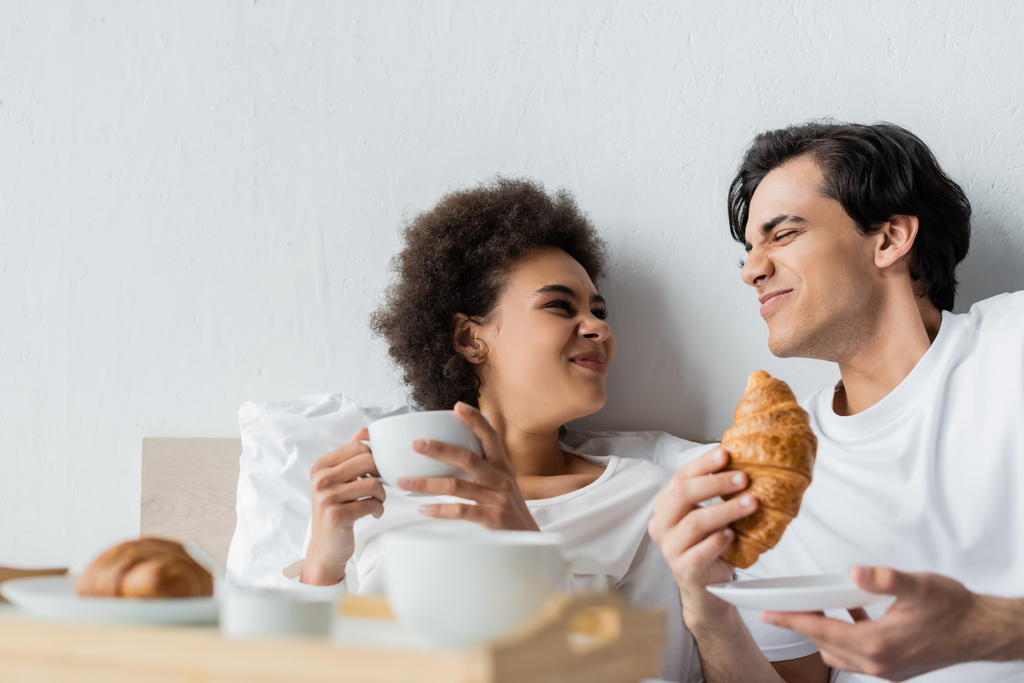 engraçado interracial casal sorrindo e enrugando narizes enquanto tendo café da manhã na cama  - Foto, Imagem