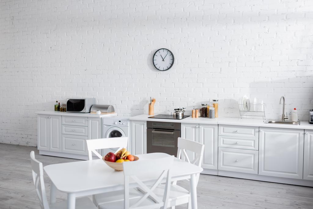 kom met vers fruit op witte eettafel in moderne keuken  - Foto, afbeelding