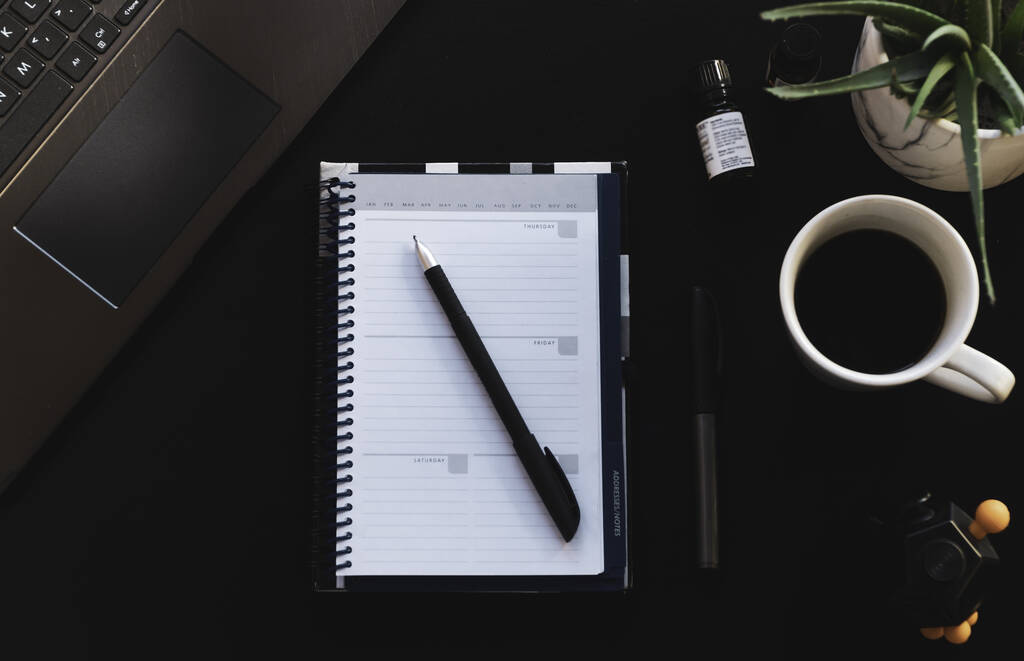 Вид зверху ручки на блокноті біля ноутбука і чашка кави
 - Фото, зображення