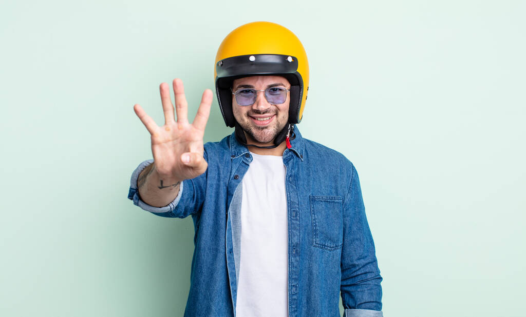 giovane bell'uomo che sorride e sembra amichevole, mostrando il numero quattro. concetto di casco moto - Foto, immagini