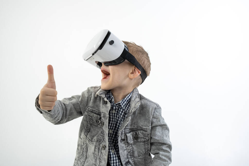 Jeune garçon avec des lunettes de réalité virtuelle isolé sur fond blanc détient geste de la main approuvant. Un enfant dans l'excitation émotionnelle portant des lunettes 3D. - Photo, image