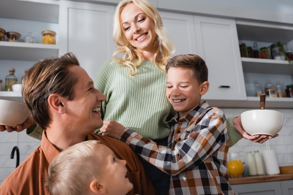 幸せな女性は台所で夫と息子の近くで朝食とボウルを保持 - 写真・画像