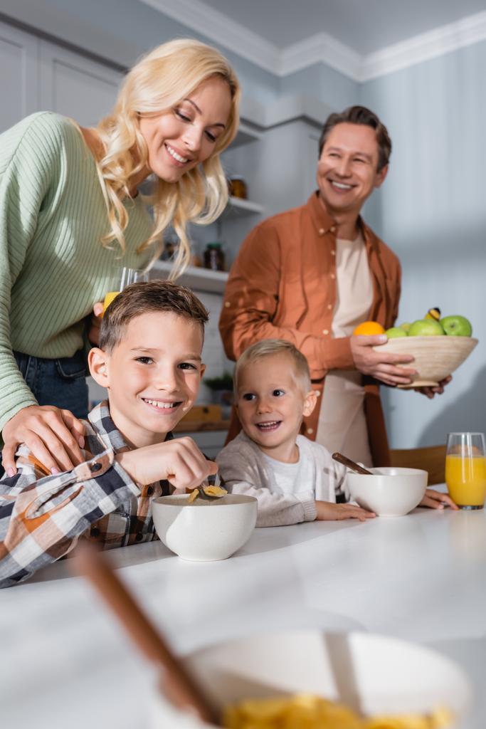 щасливі брати їдять кукурудзяні пластівці біля щасливих батьків на кухні
 - Фото, зображення