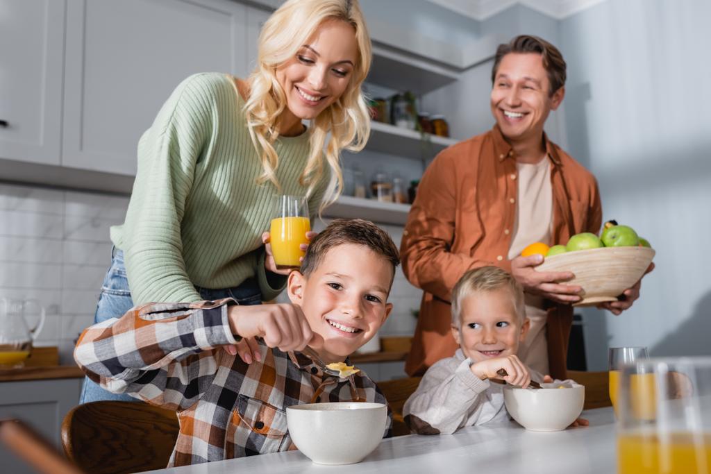 freudige Brüder essen Müsli zum Frühstück in der Nähe der Eltern mit frischem Obst und Orangensaft - Foto, Bild