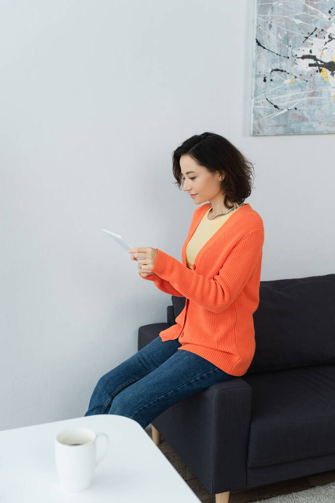 Nuori nainen, joka käyttää digitaalista tablettia ja nojaa sohvalla  - Valokuva, kuva