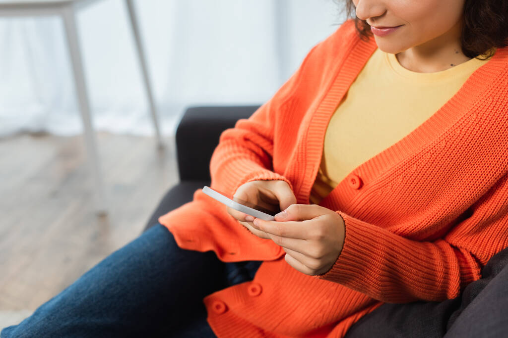 kivágott kilátás fiatal nő sms-ező mobiltelefon a nappaliban  - Fotó, kép
