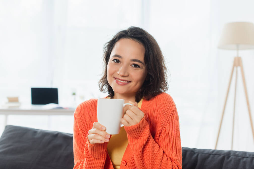 Feliz joven mujer sosteniendo taza en casa  - Foto, Imagen