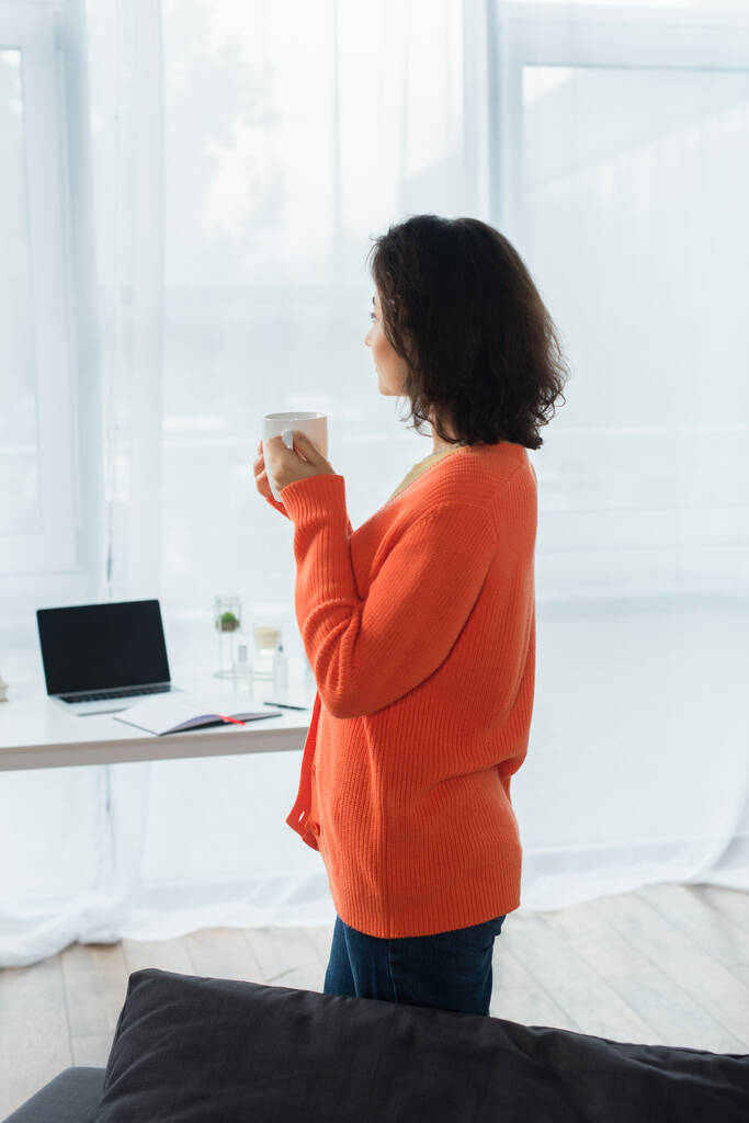 boční pohled na mladou ženu držící šálek kávy doma - Fotografie, Obrázek