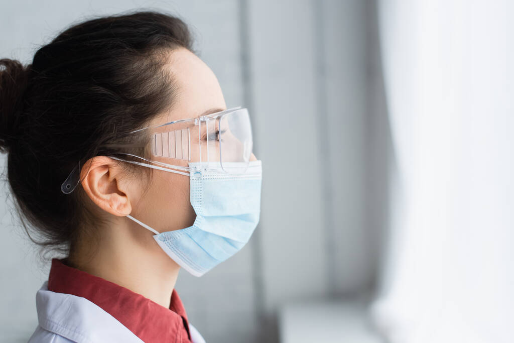 zijaanzicht van brunette wetenschapper in bril en medisch masker  - Foto, afbeelding