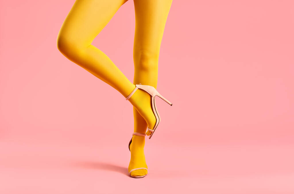 Sarı taytlı, yüksek topuklu ayakkabılı, ince bacaklı genç bir kadın bir ayağının üzerinde dengede duruyor. - Fotoğraf, Görsel