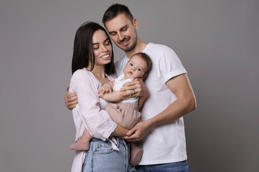 Una famiglia felice. Coppia con il loro bambino carino su sfondo grigio - Foto, immagini