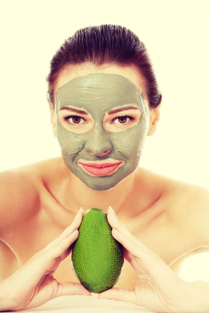 Bella donna con maschera facciale in possesso di avocado
. - Foto, immagini